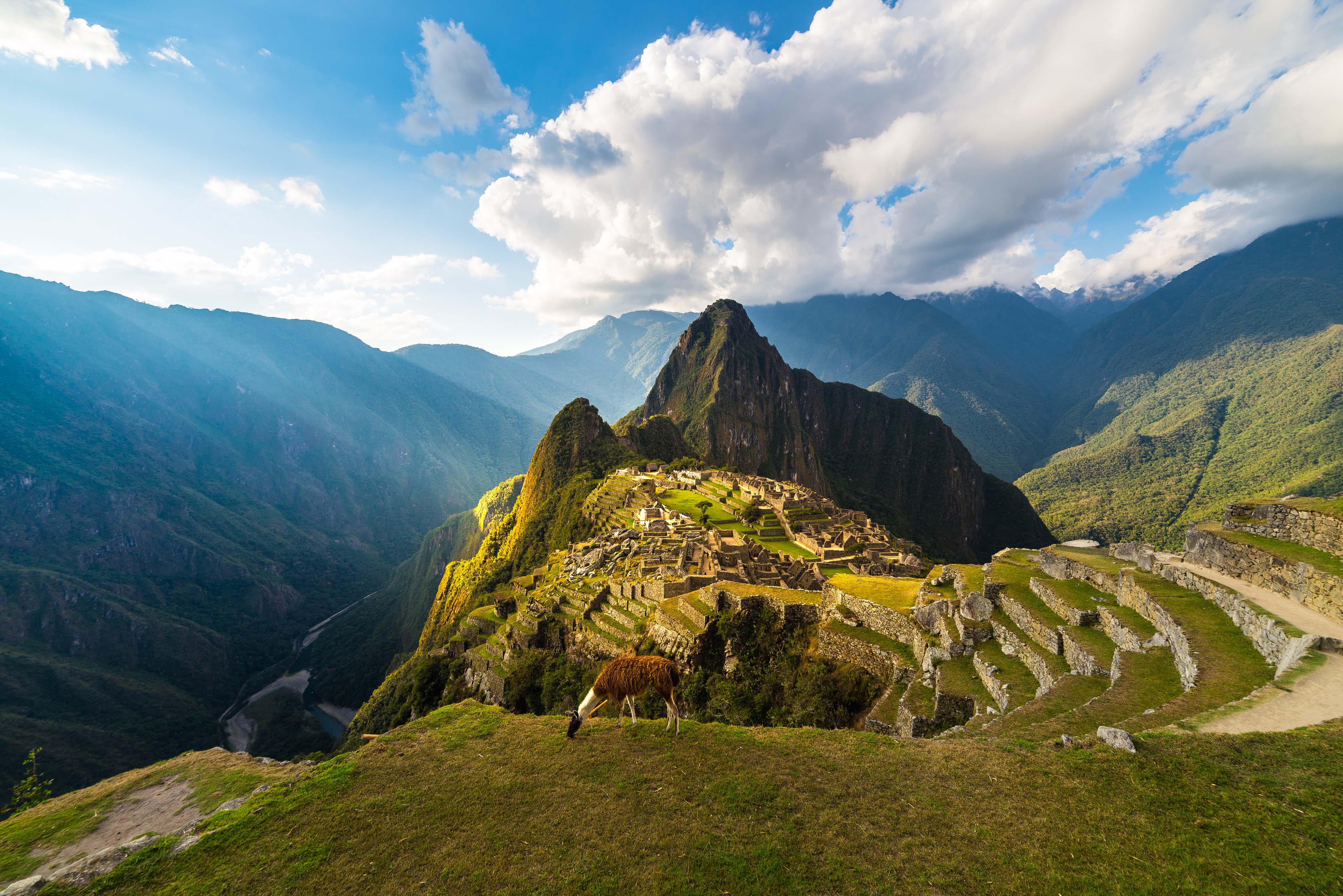 3862x2578 Machu Picchu illuminated by the warm sunset light. Wide angle view from the terraces above with scenic sky and sun burst. Dreamlike travel destination, world wonder. Cusco Region, Peru