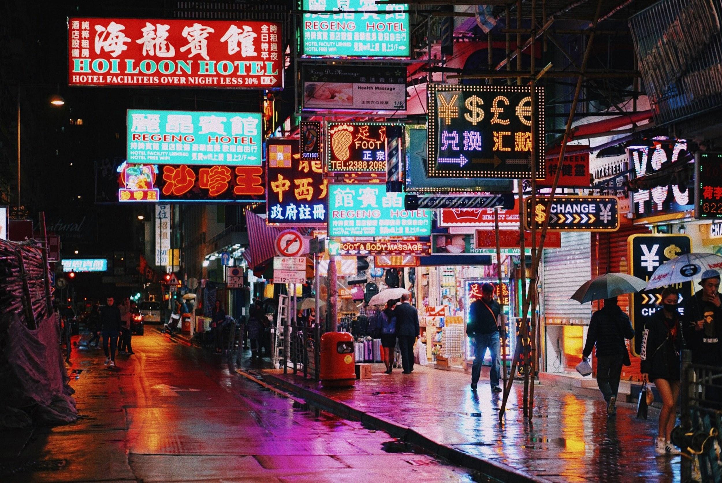 2500x1671 Wallpaper / night time scene of a city street with several neon lights and signs over people walking around with umbrellas in a hong kong urban region, hong kong neons