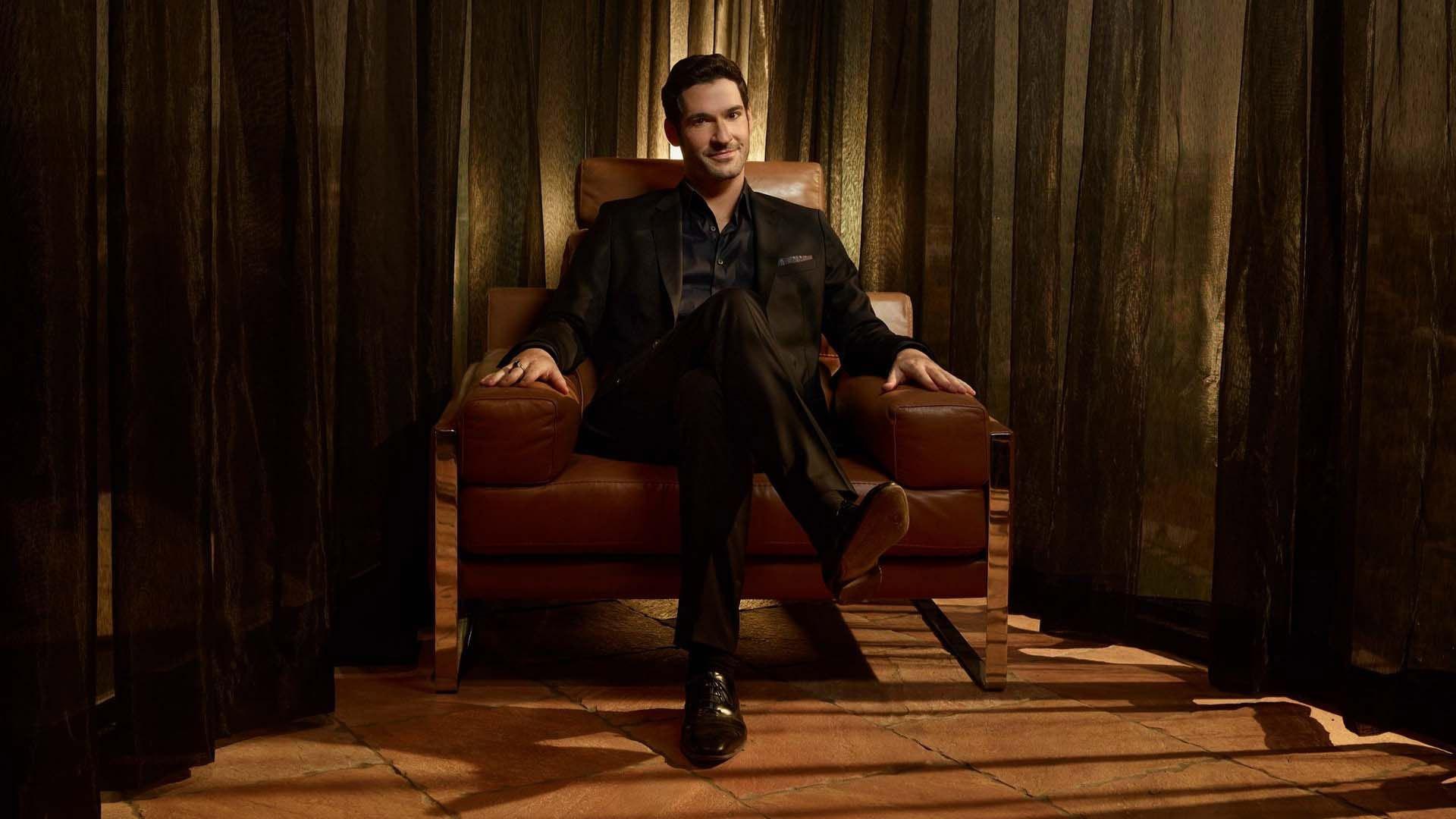 1920x1080 Tom Ellis Is Wearing Black Coat Suit Sitting On Brown Couch HD Lucifer Wallpaper
