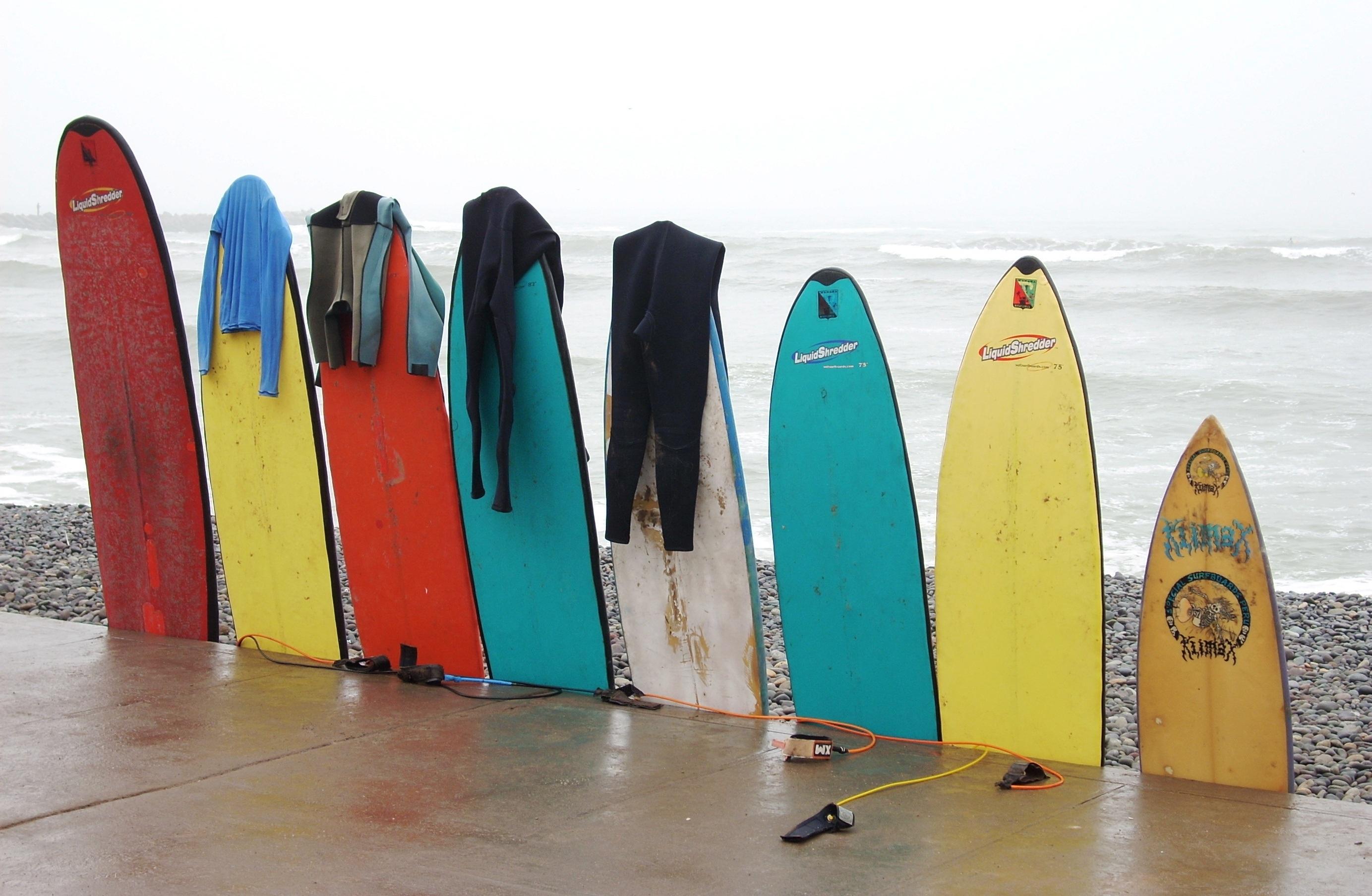 2767x1807 A row of surfboards with wetsuits hanging off them HD Wallpaper