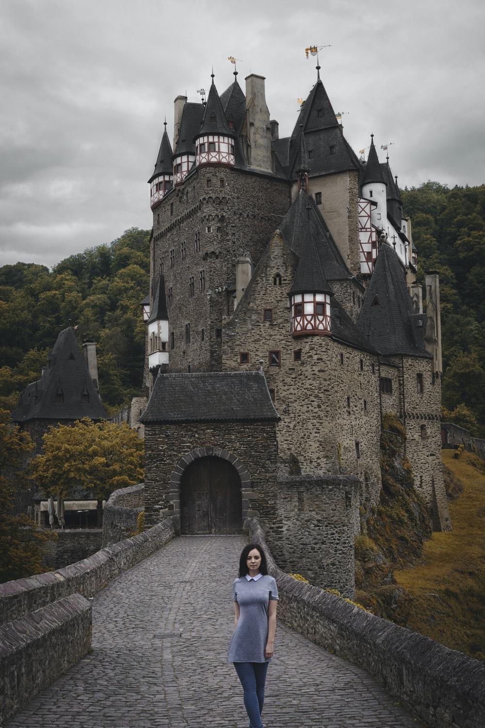 1000x1500 woman walking near gray ancient castle surrounded with tall and green trees photo