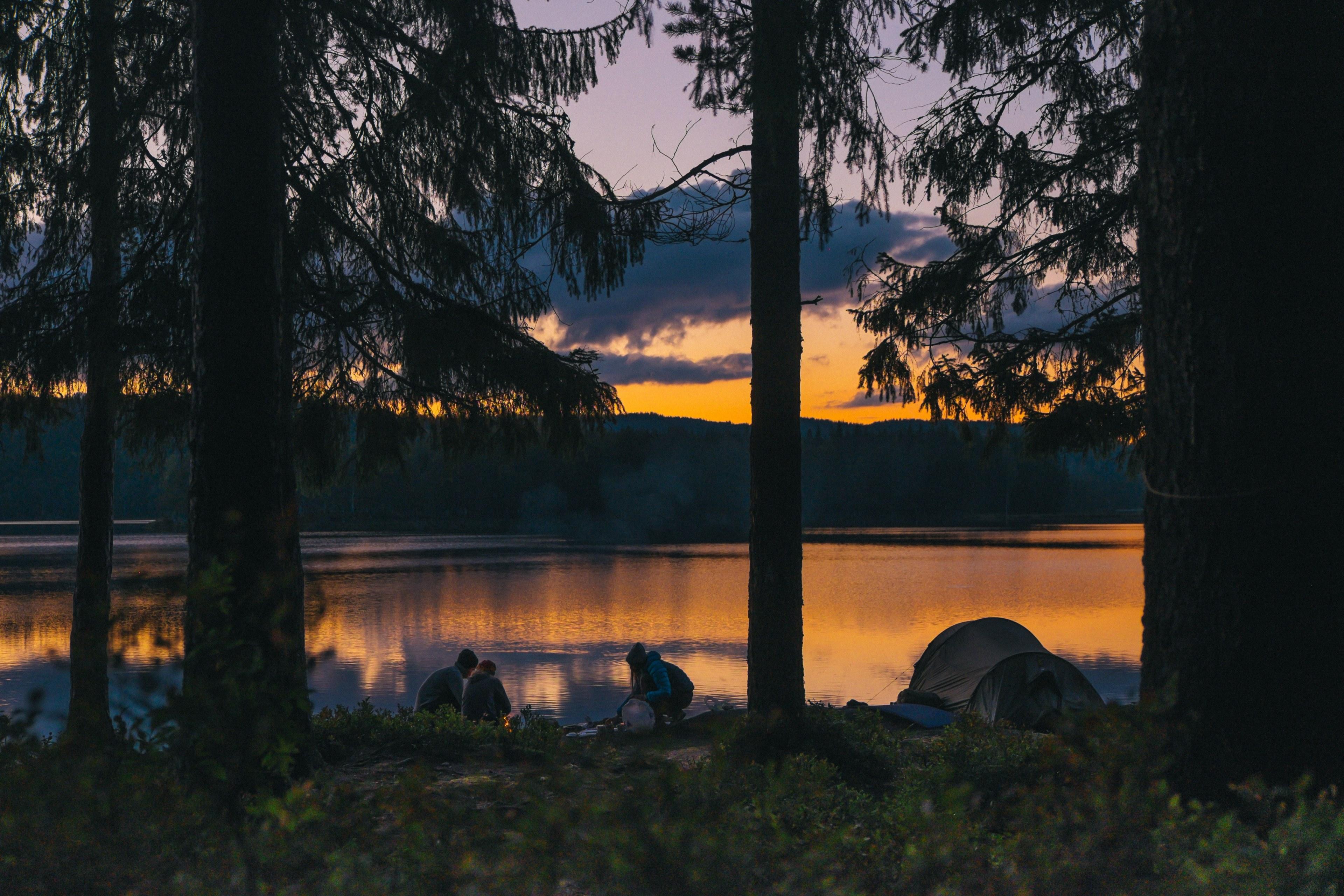 3840x2560 Wallpaper / people camping with a gold sunset through forest trees at a tranquil lake that reflects the warm light, camping at sunset_ 4k wallpaper