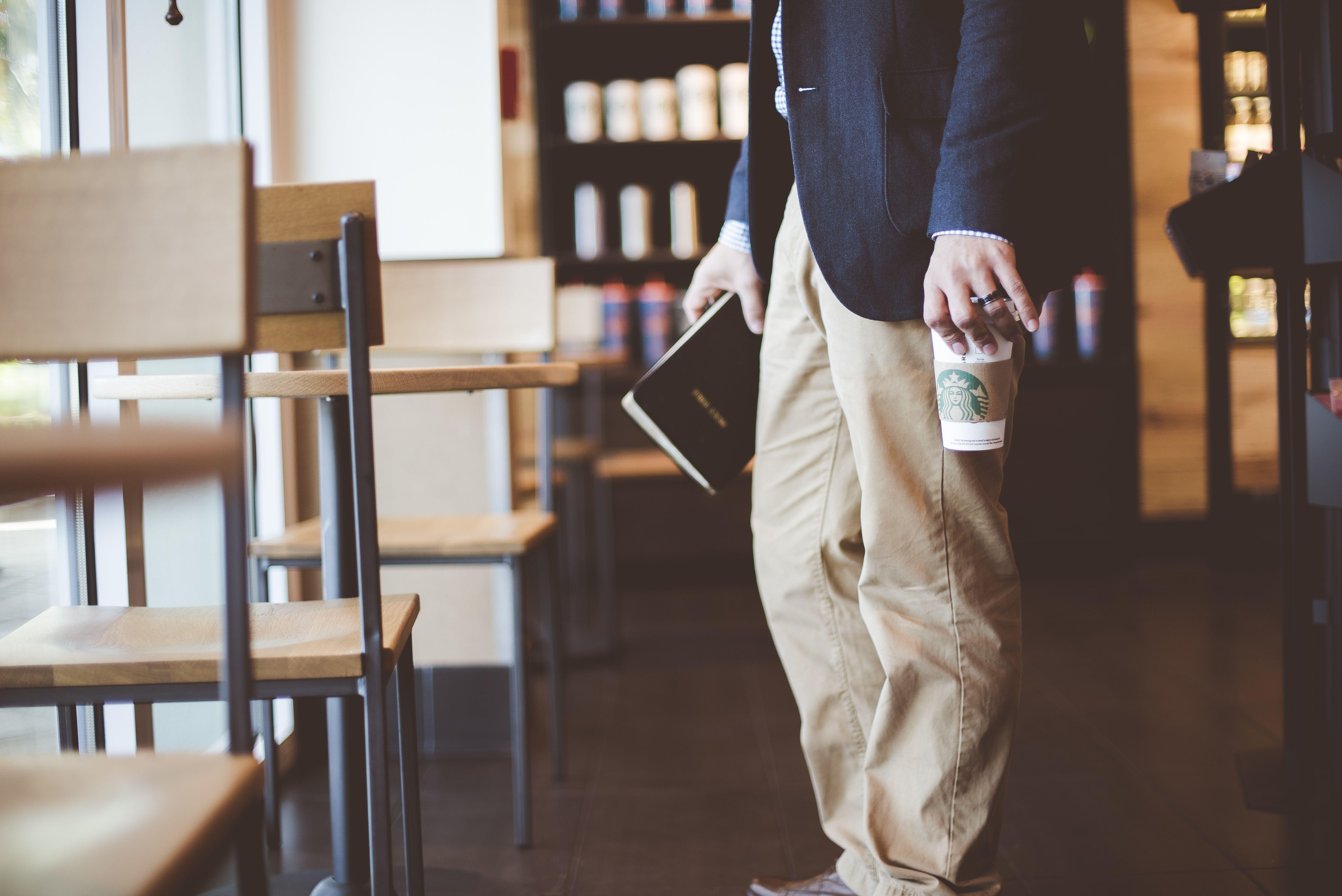 6016x4016 person holding starbucks disposable cup near table set inside