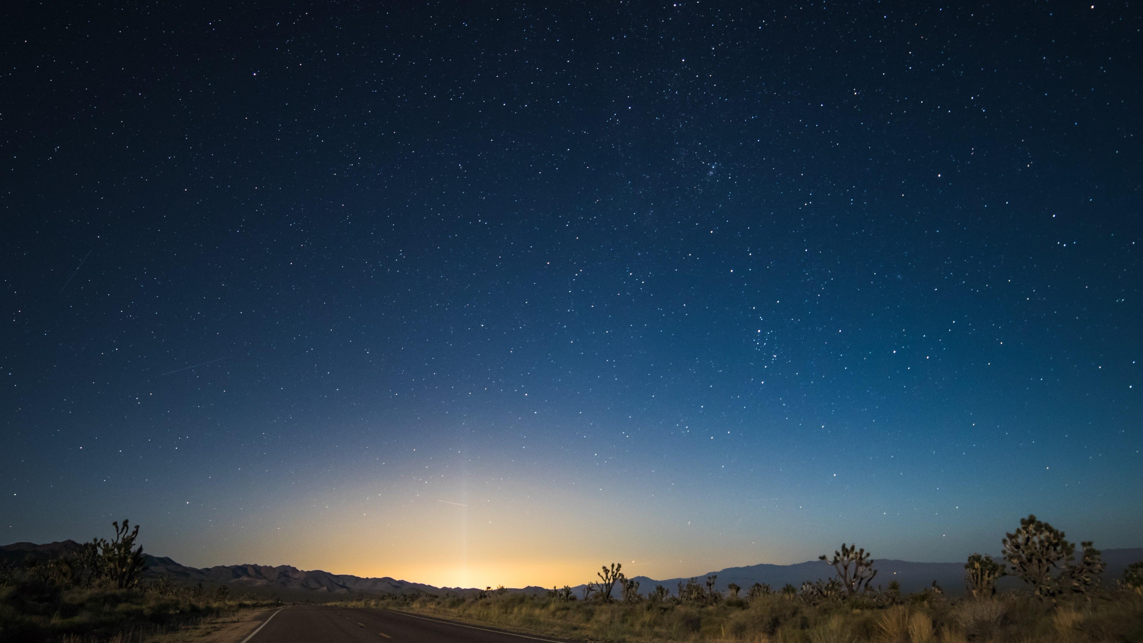 3840x2160 Wallpaper / the pavement in the center of desert area leads to glowing sunrise illuminating night sky, starry sky transition at nipton 4k wallpaper free download