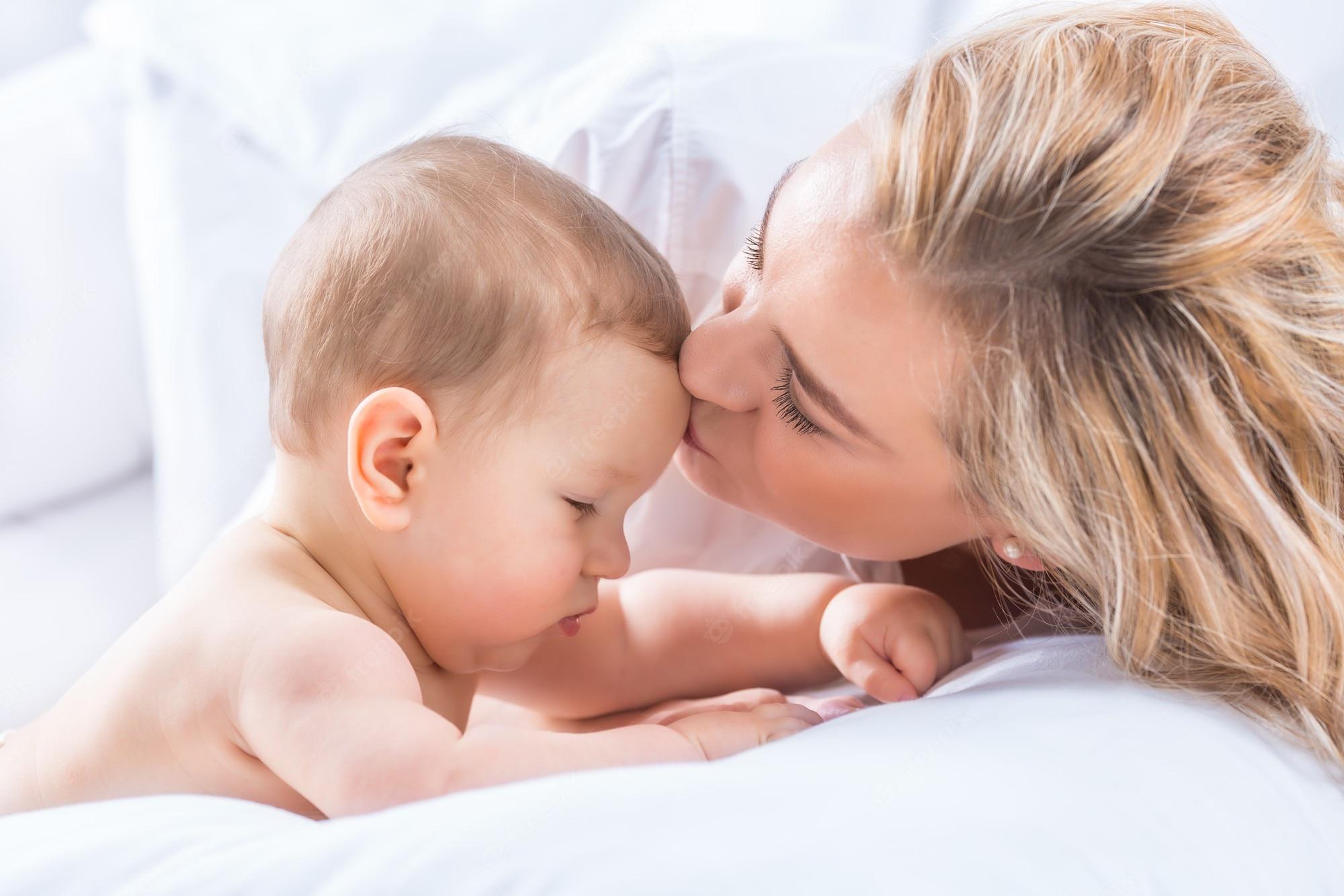 2000x1333 Premium Photo. Mother and baby boy son playing on a white bed. mothers tenderness and kisses of a toddler child