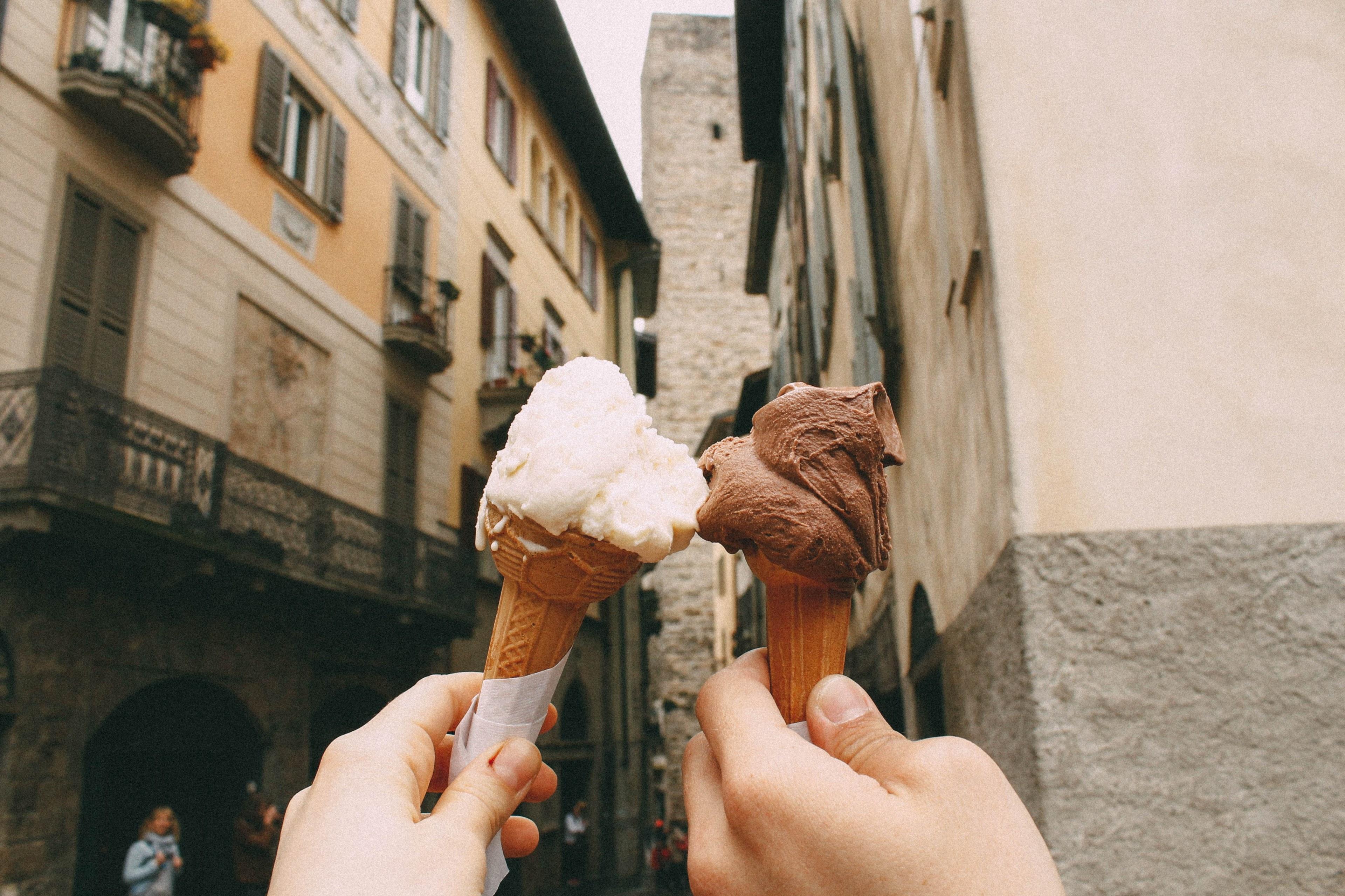 3840x2560 Wallpaper / man and woman hold up chocolate and vanilla ice cream cones in old side street, outside the ice cream shop 4k wallpaper free download