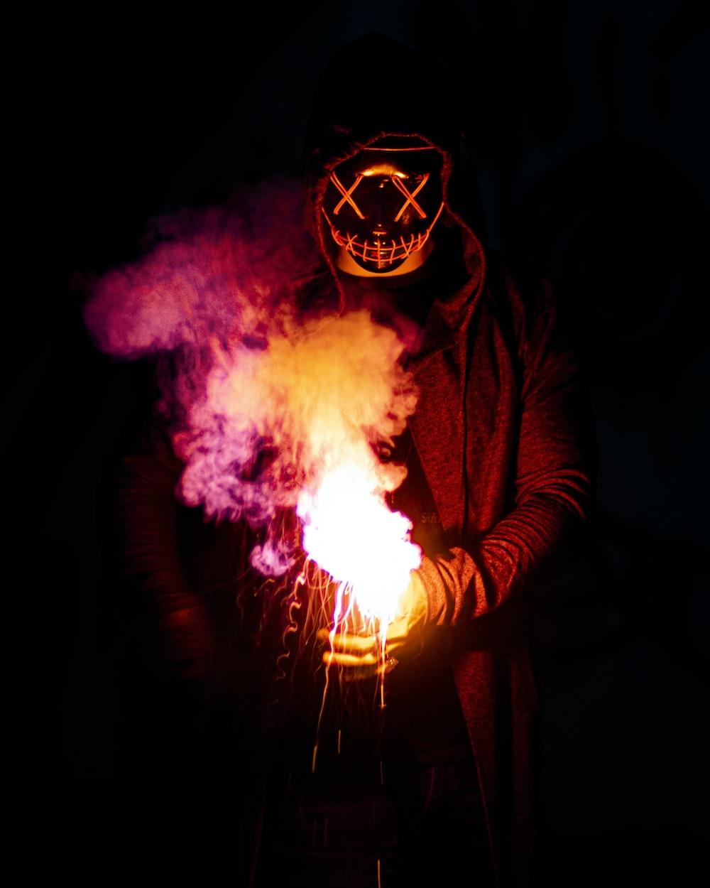 1000x1250 person in black mask holding purple and pink smoke photo