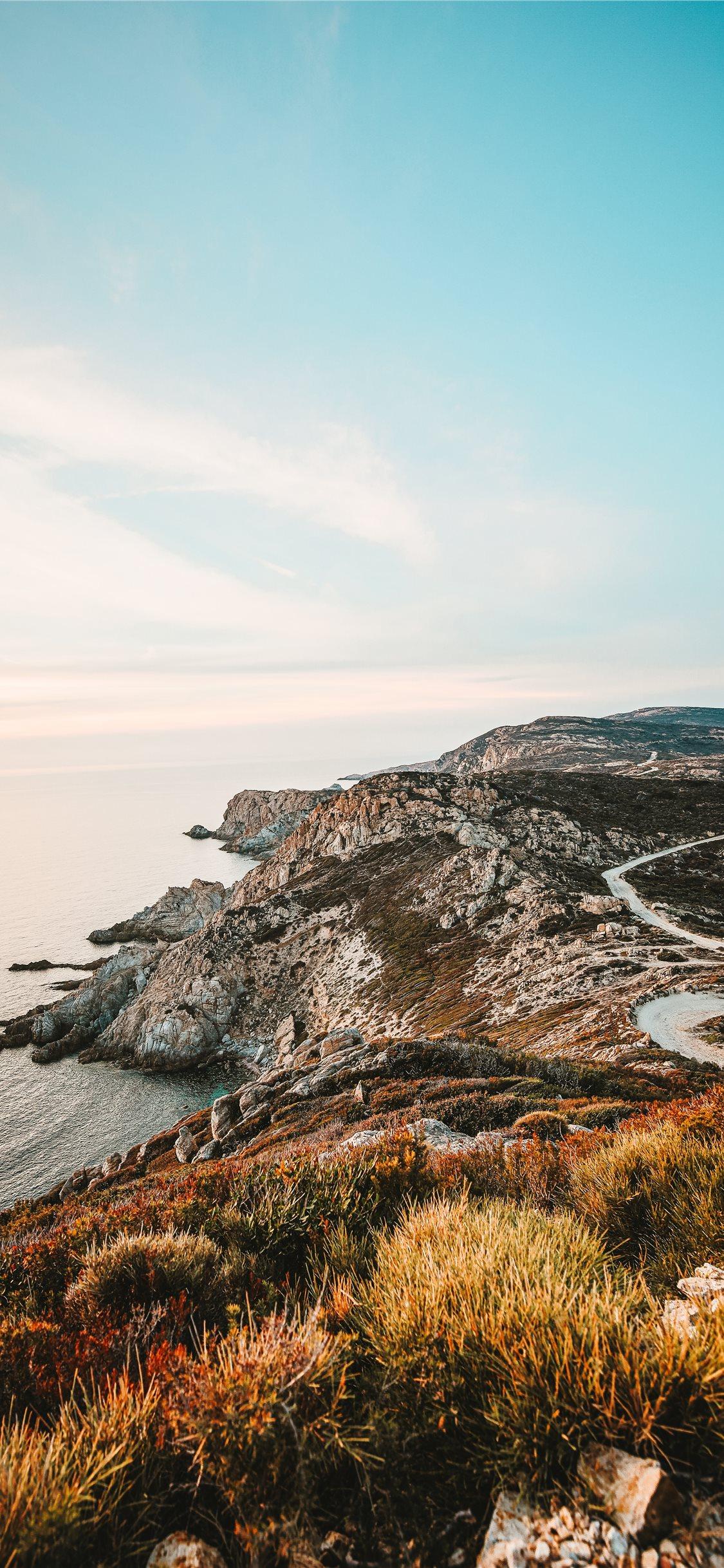 1125x2436 rocky cliff facing ocean under blue sky iPhone X Wallpaper Free Download