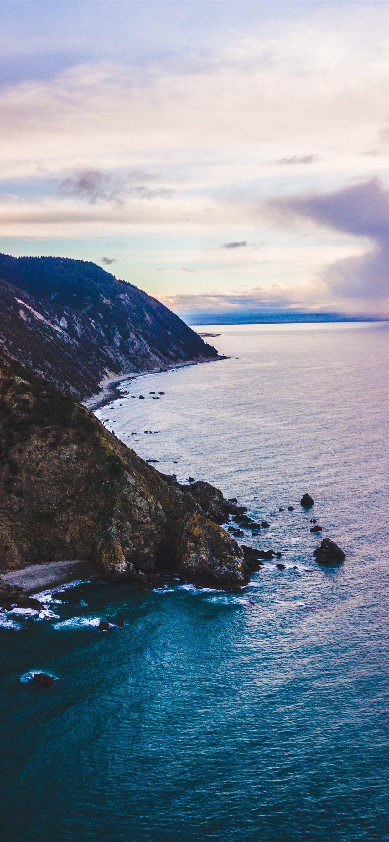 1242x2688 calm body of water crashing on shore of cliff unde. iPhone X Wallpaper Free Download
