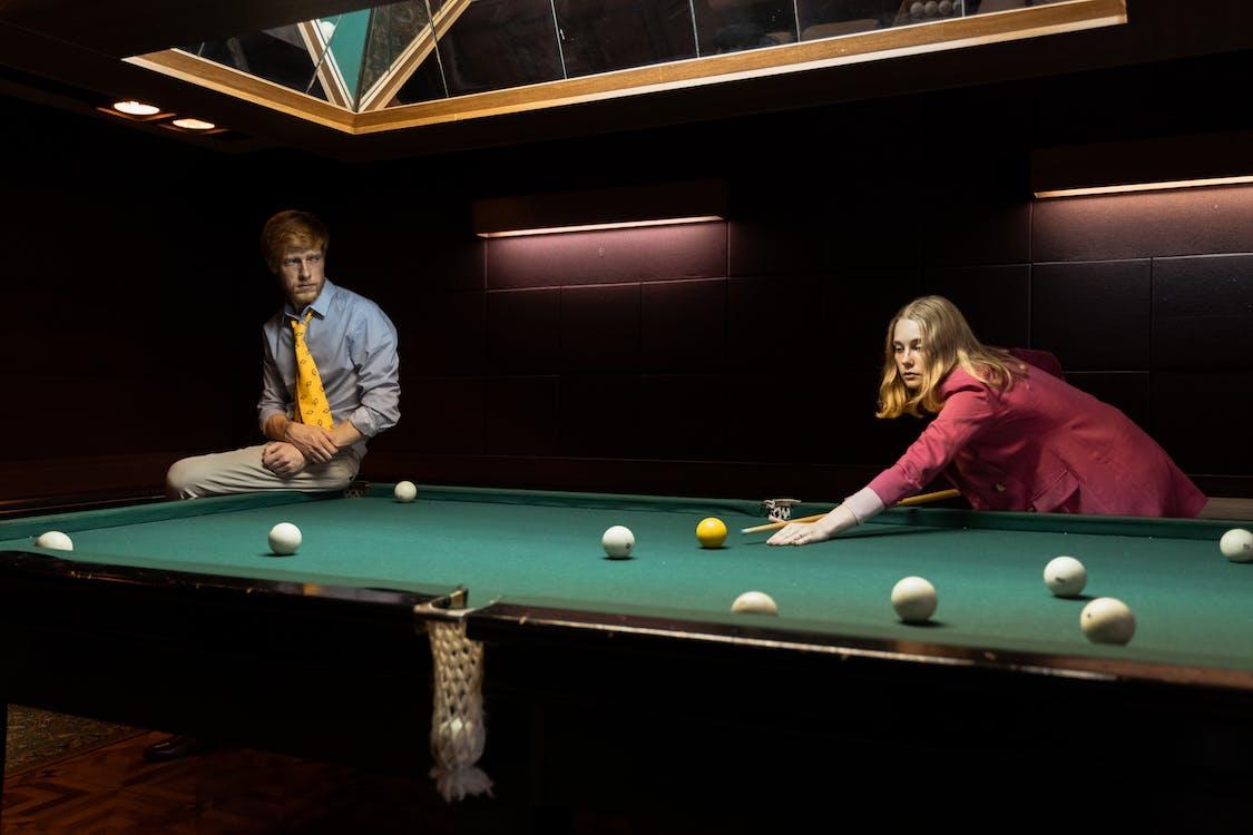 1125x750 A Man Siting on a Billiard Table Looking at a Woman Playing Billiards · Free