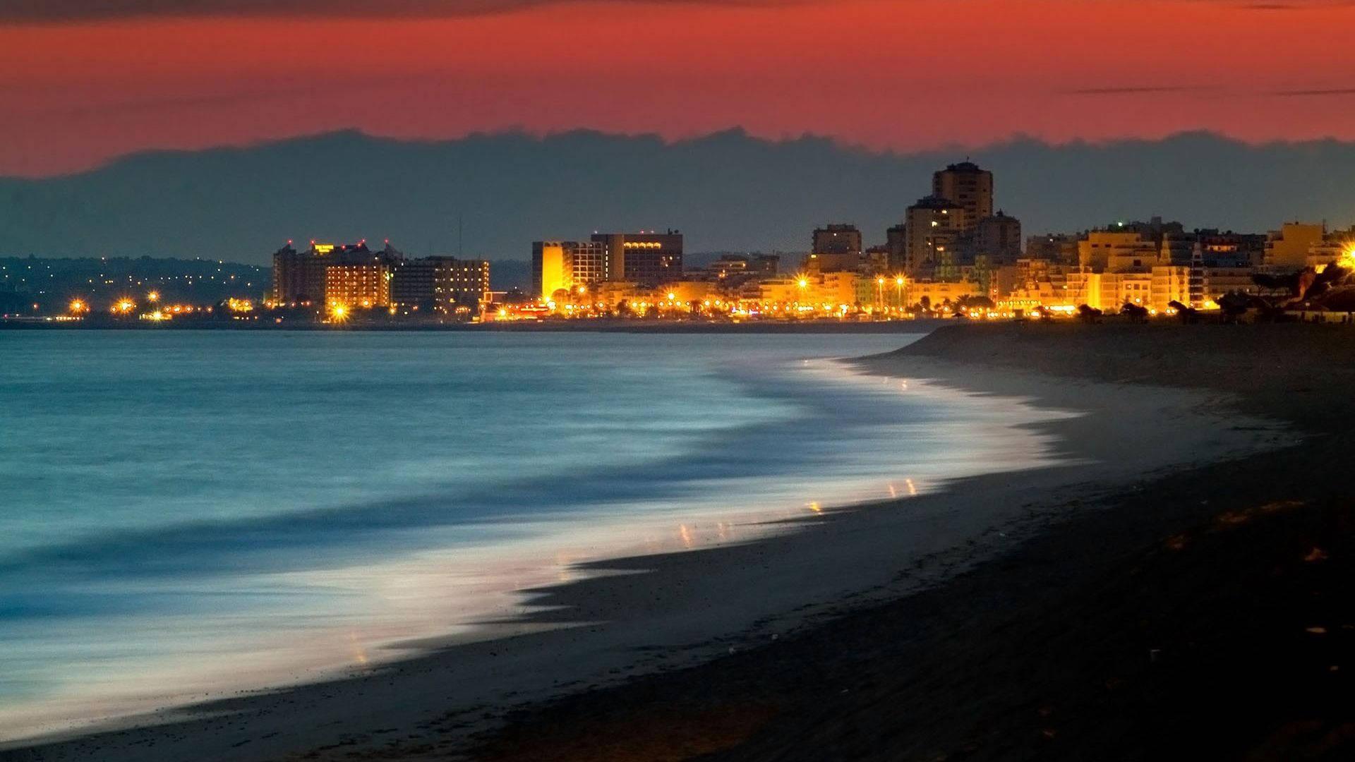 1920x1080 Download A City At Night With A Beach And Ocean Wallpaper