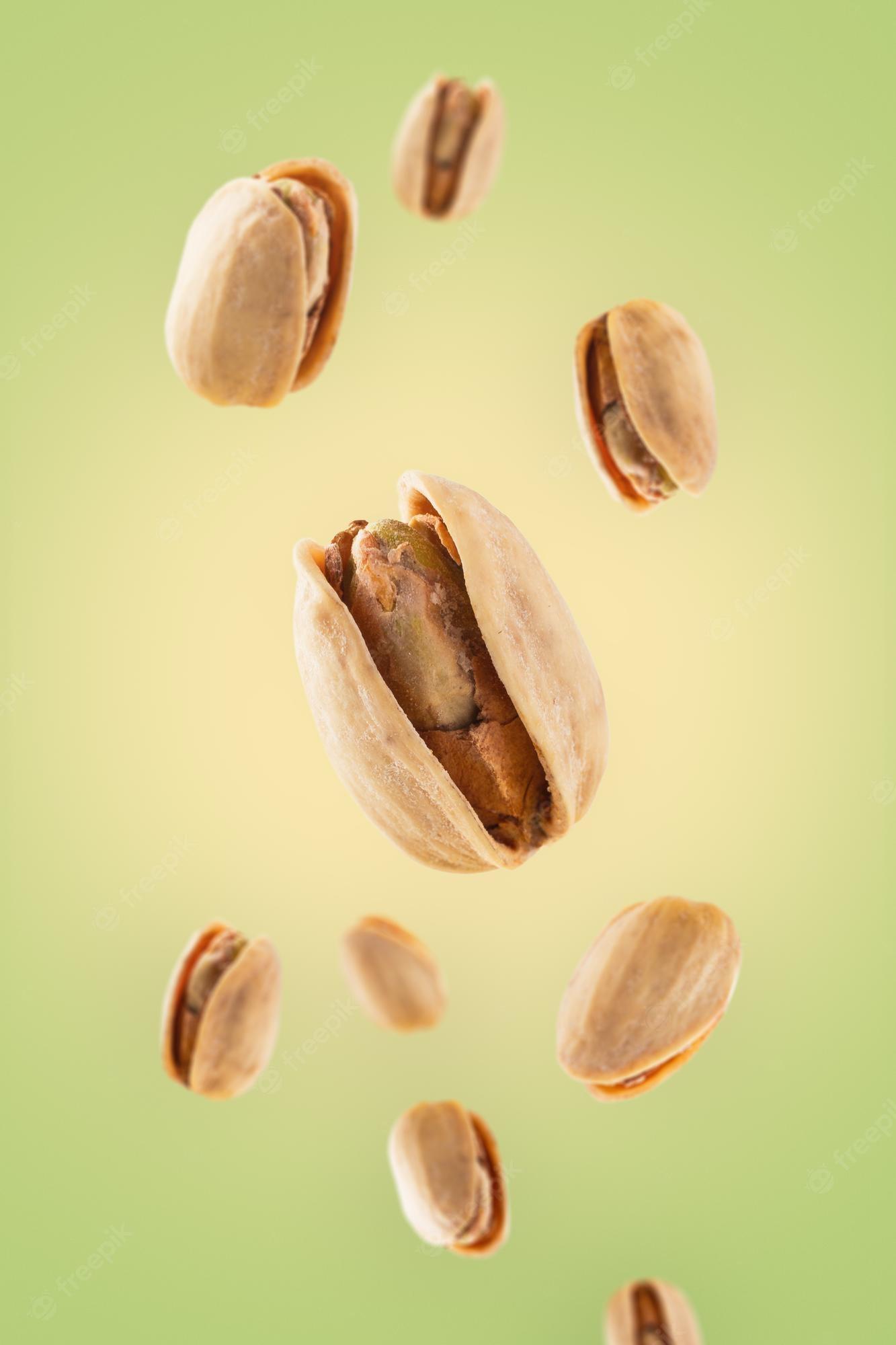 1333x2000 Premium Photo. Wallpaper of roasted pistachios floating on light green and yellow background