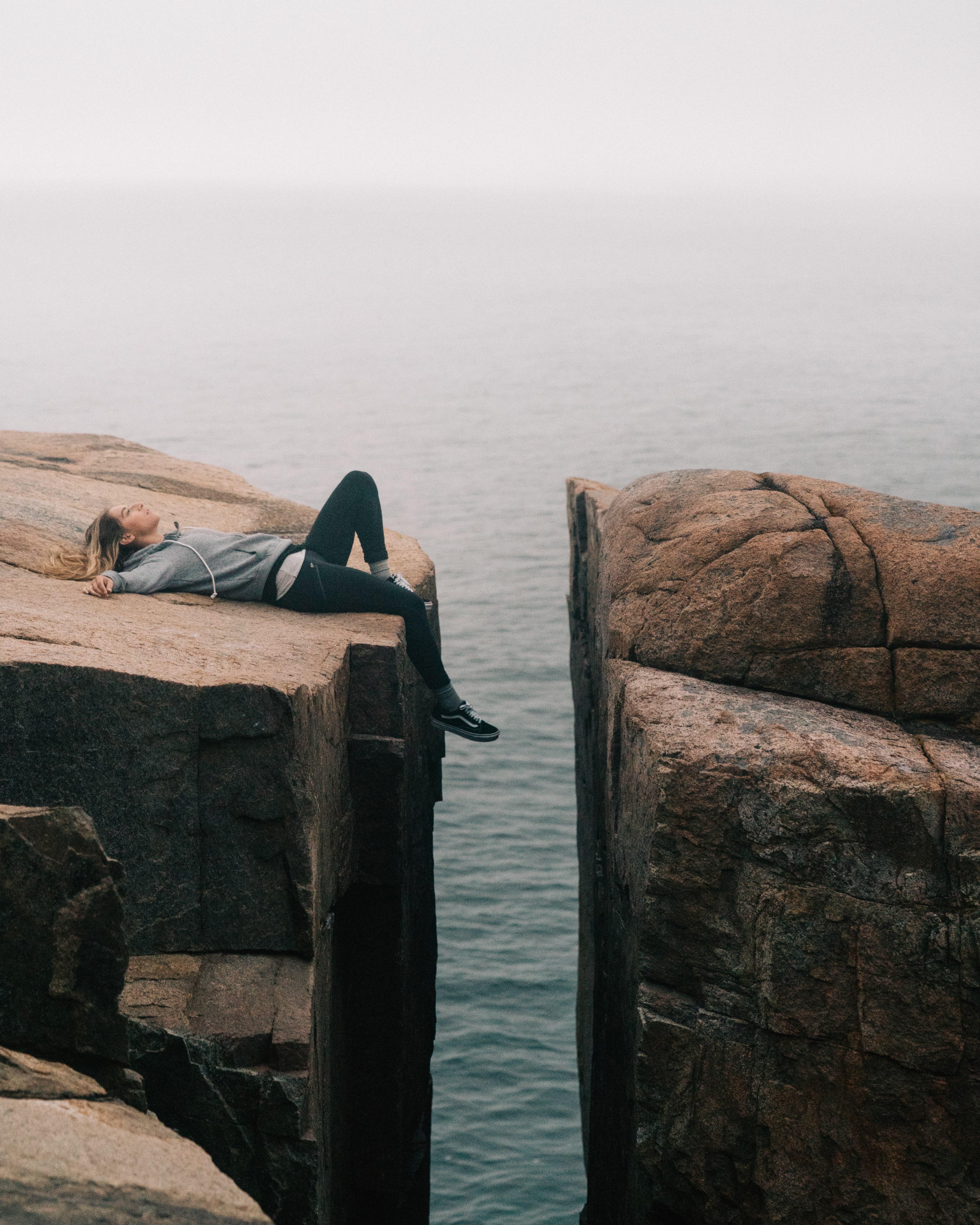 3840x4800 Wallpaper / a woman laying down on her back with her feet dangling between two massive rocks over the sea, on the edge of the world 4k wallpaper free download