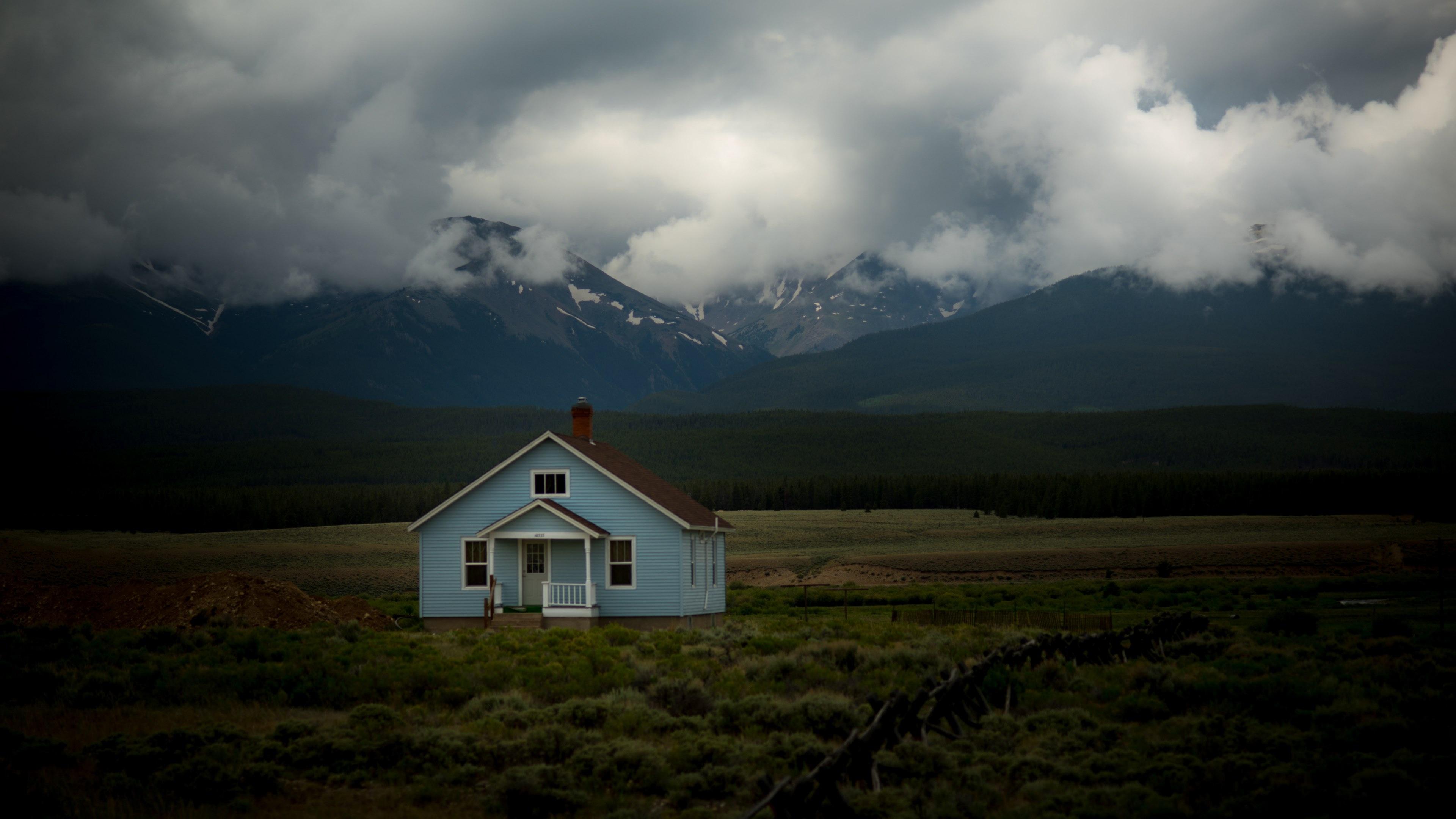3840x2160 Wallpaper / small blue house in the middle of a field of grass with mountains covered in clouds behind it, blue house in field 4k wallpaper free download
