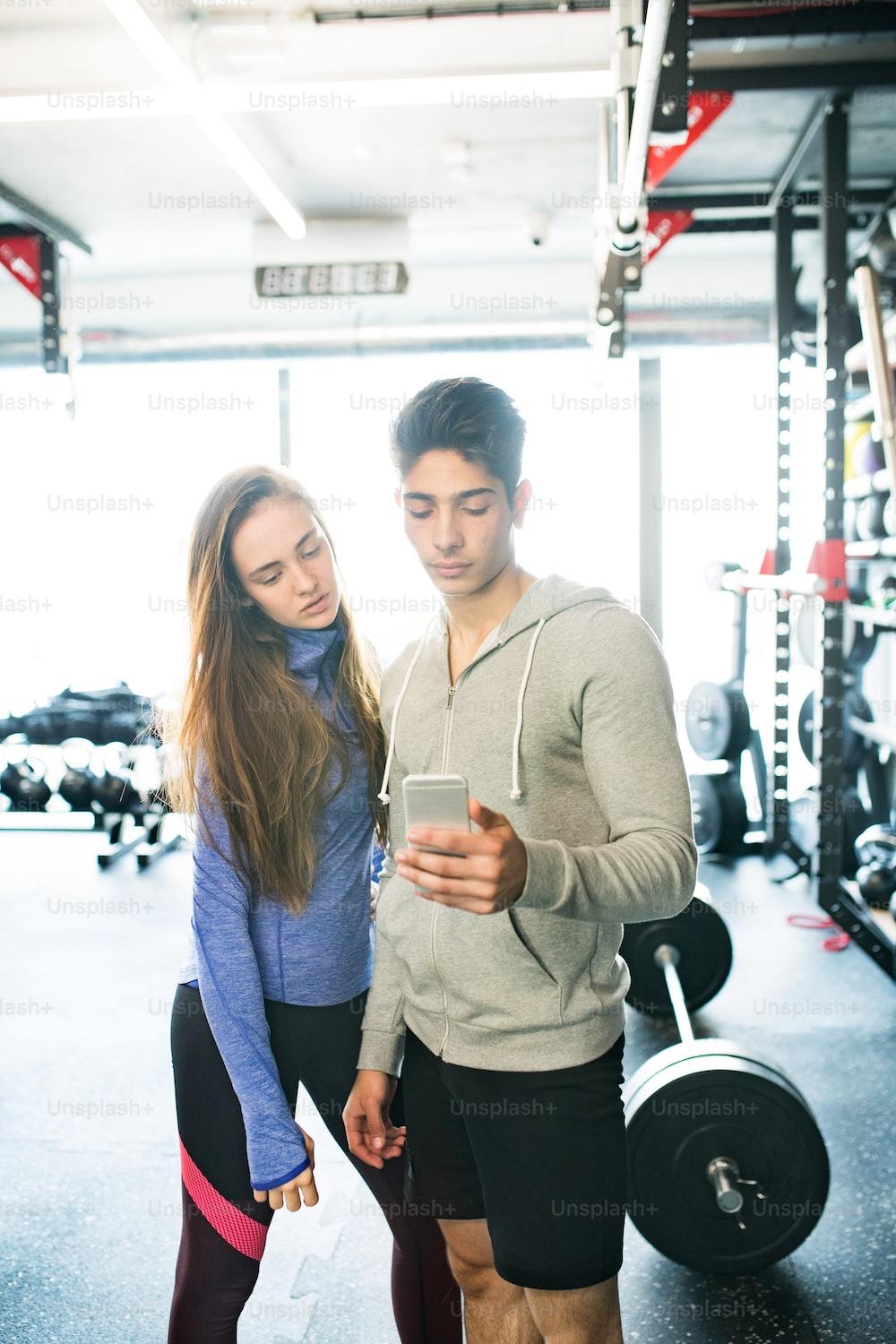 1000x1500 Beautiful young fit couple in modern gym holding smart phone, posing. photo