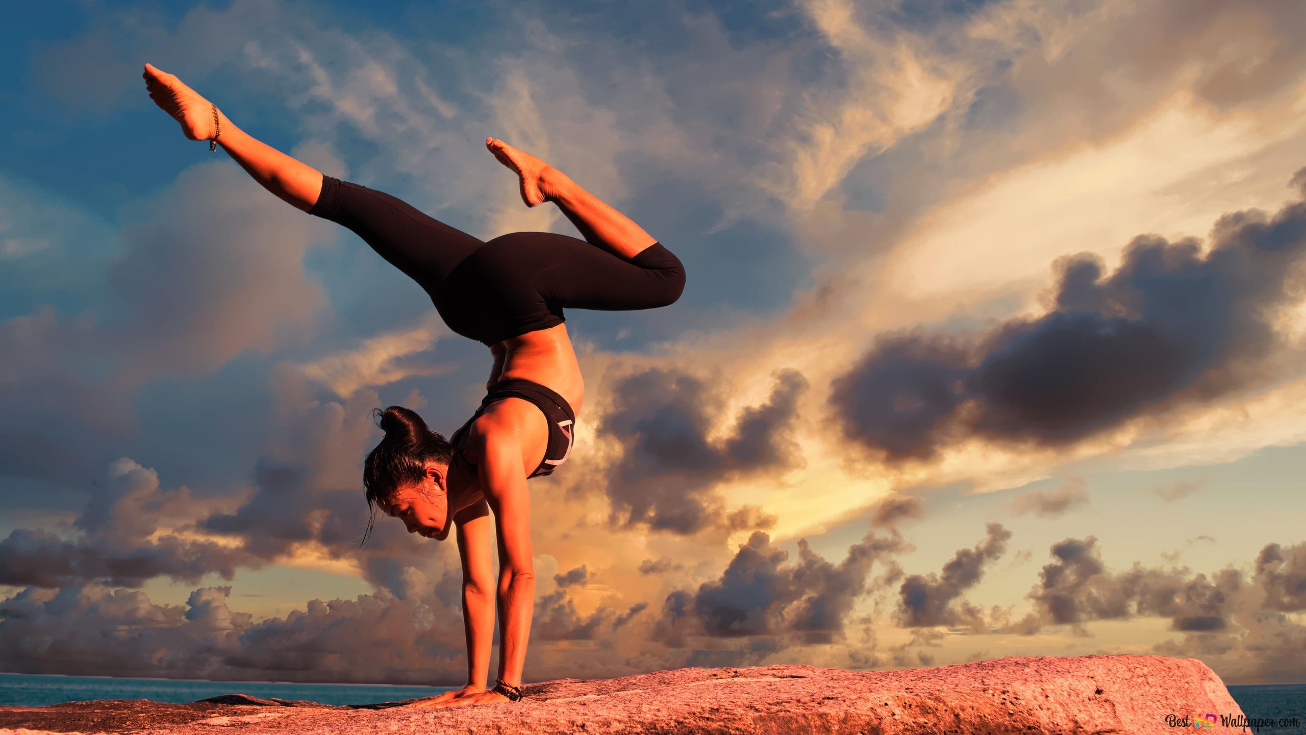 2560x1440 Woman in sportswear doing yoga on rock by the sea and cloud view 4K wallpaper download