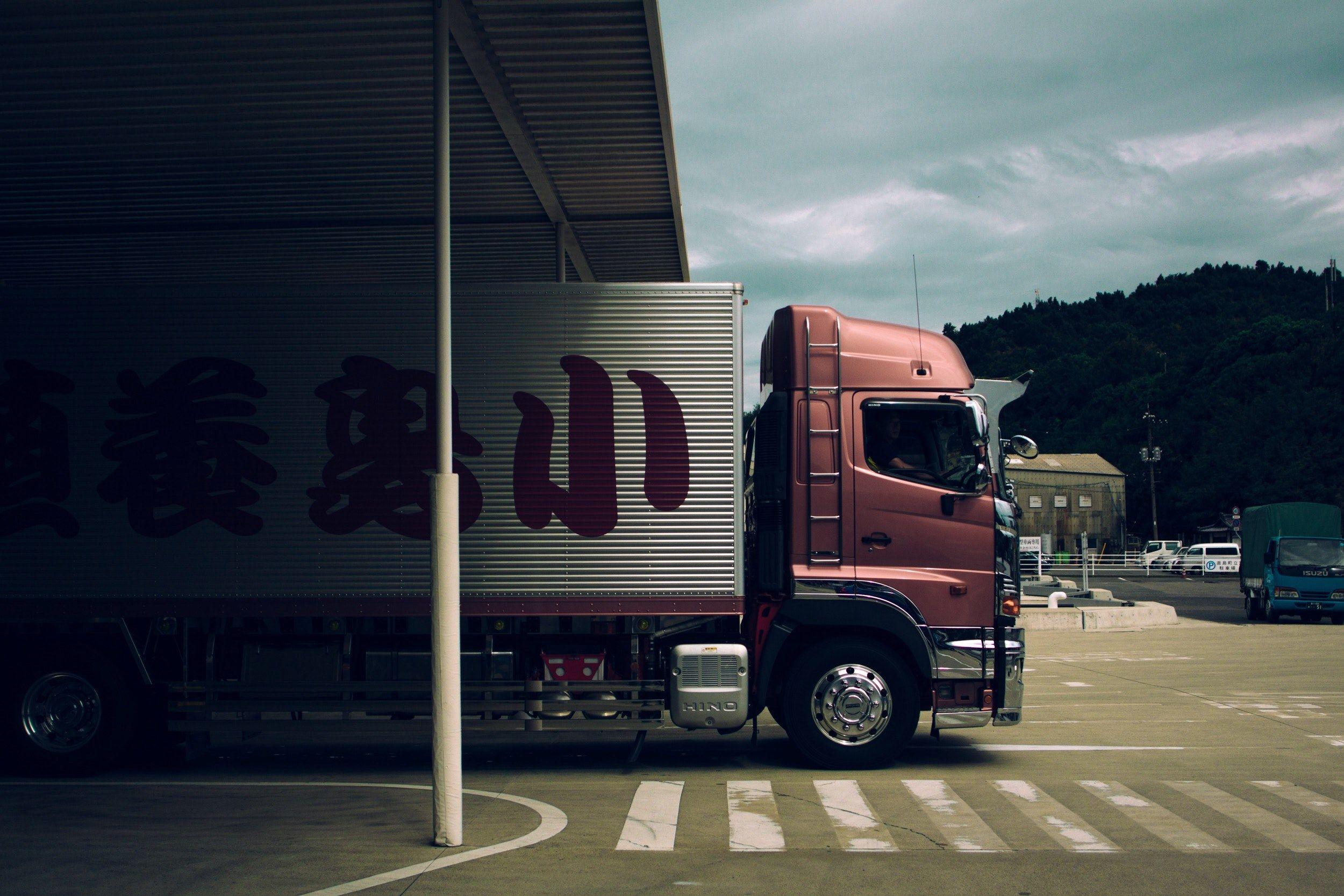 2500x1667 Wallpaper / a pink truck with japanese lettering on its container exiting a roofed area beside a hill of trees, pink japanese truck 4k wallpaper free download