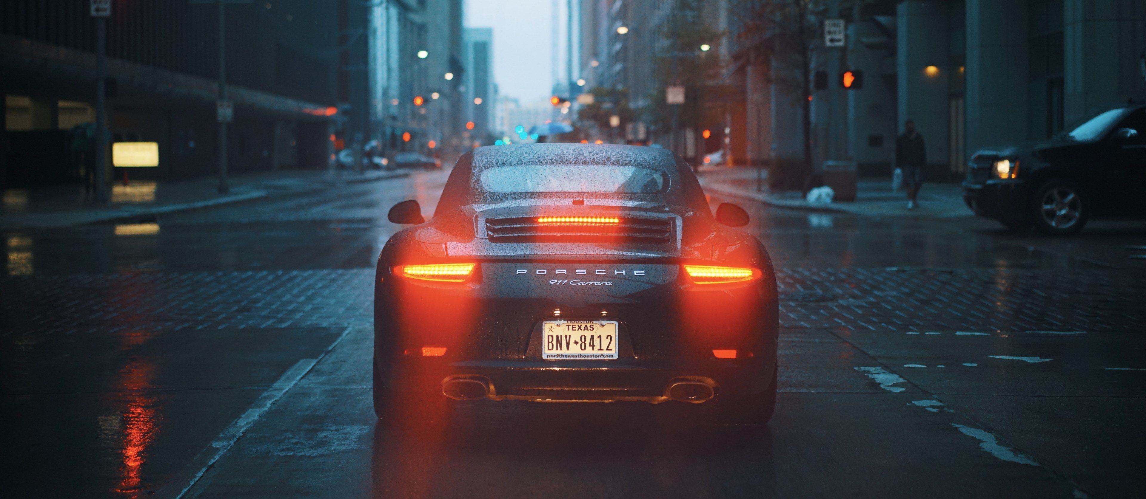 3840x1674 Wallpaper / the back of a black porsche 911 with its tail lights on on a wet street, porsche 911 on a rainy evening 4k wallpaper free download