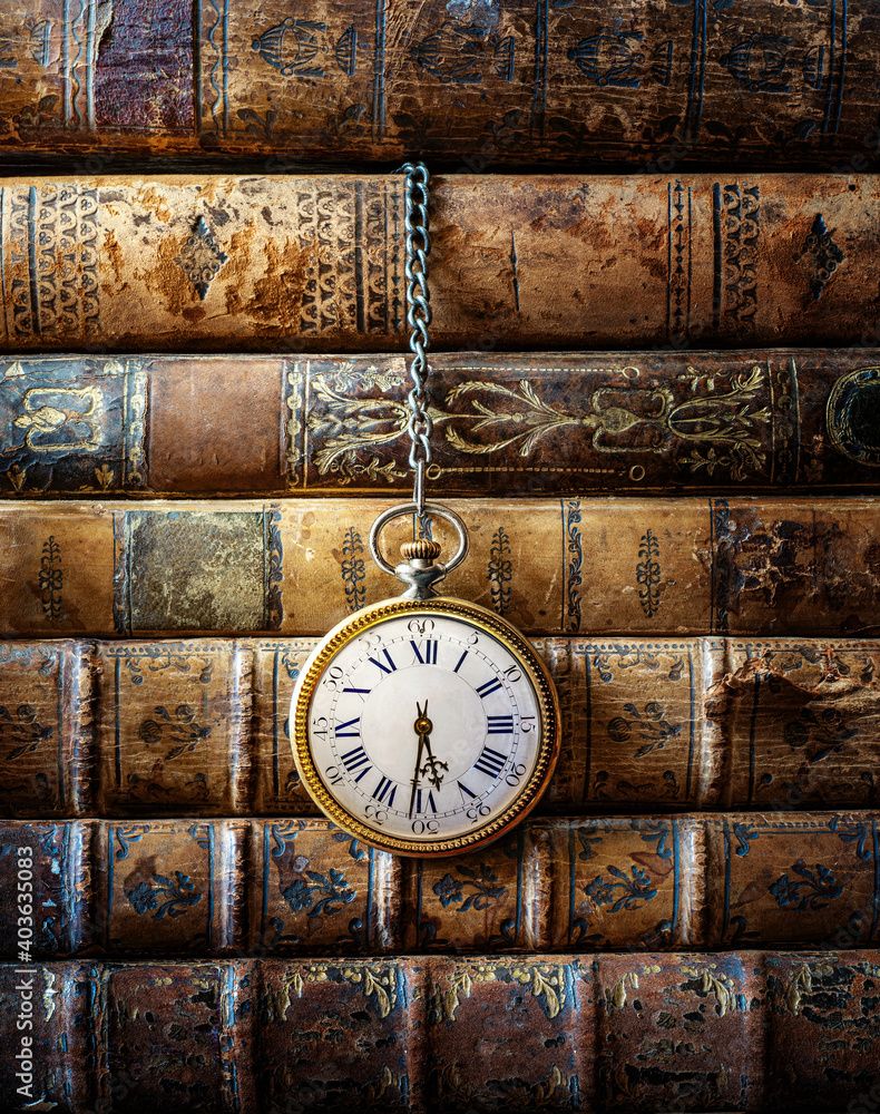 790x1000 Vintage clock hanging on a chain on the background of old books. Old watch as a symbol of passing time. Concept on the theme of history, nostalgia, old age. Retro style. Stock