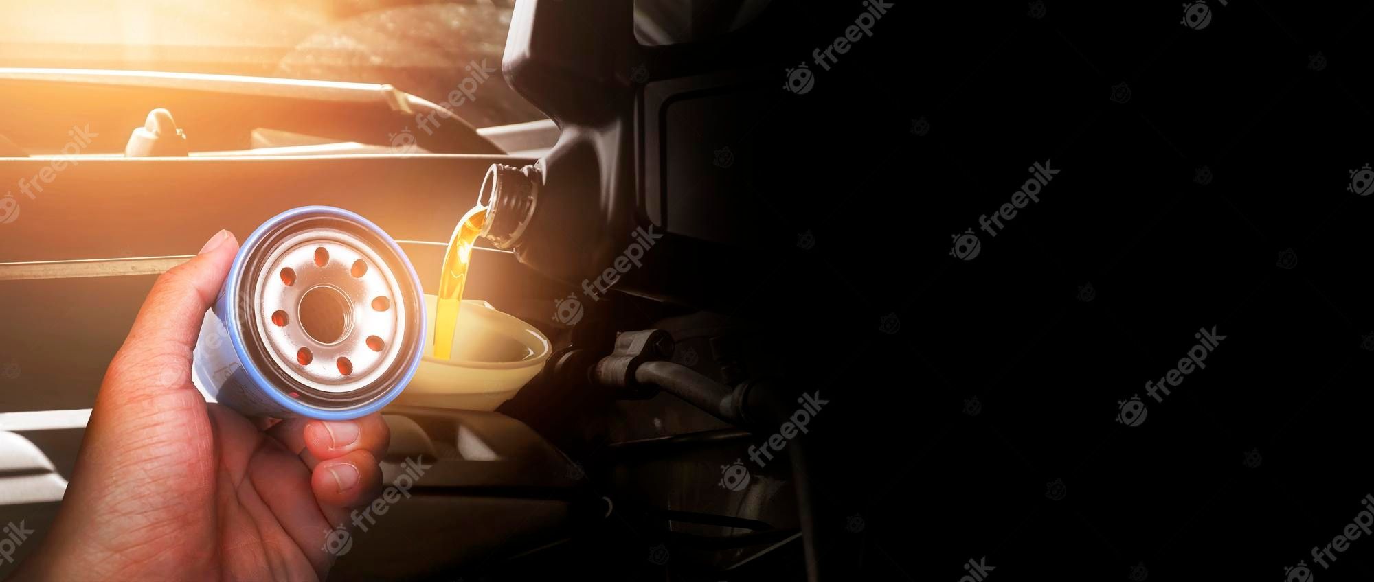 2000x848 Premium Photo. Mechanic hand showing oil filter against the background pouring motor oil into the car engine in the engine compartment panoramic banner with copy space on black background