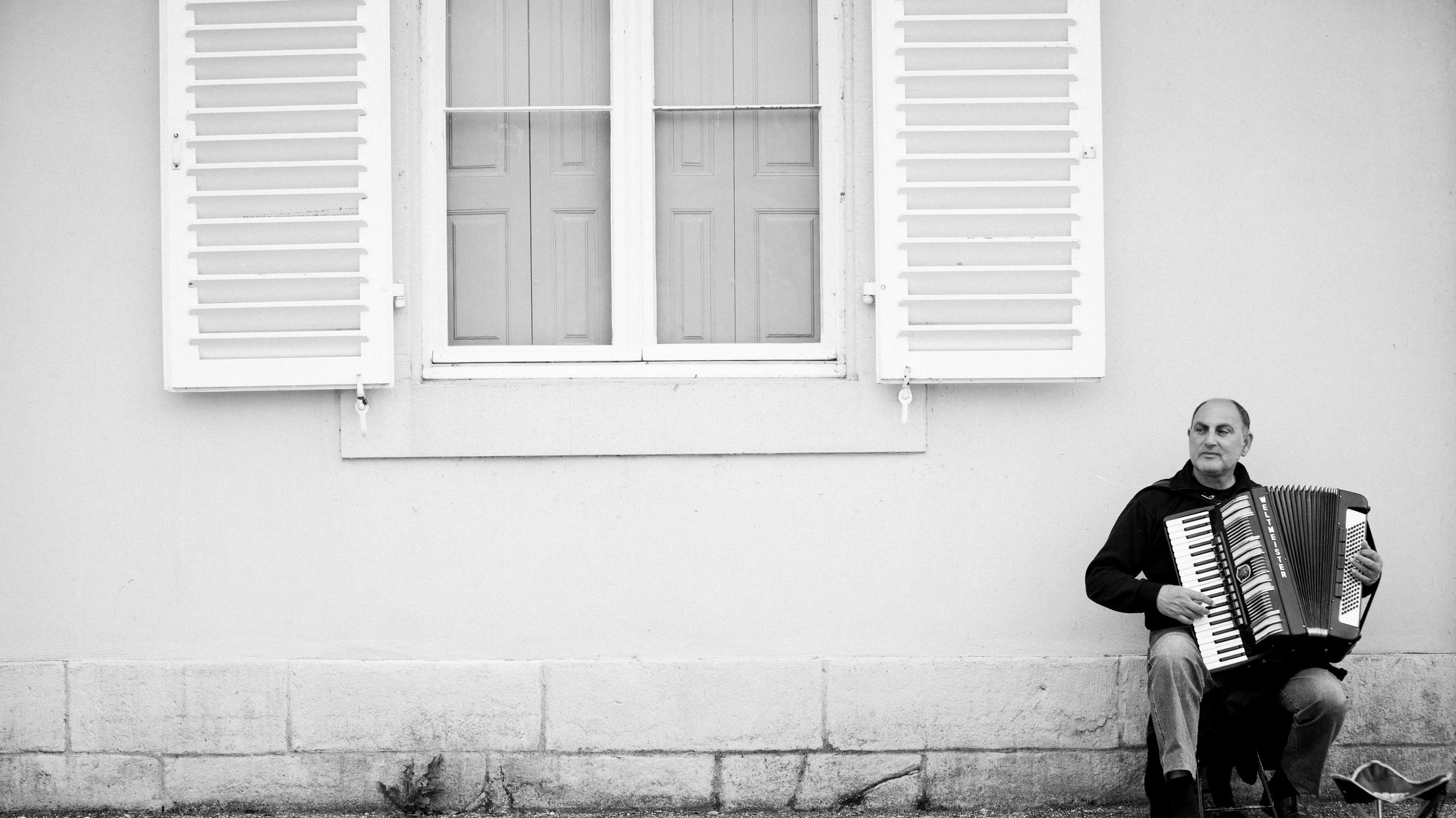 2560x1440 Wallpaper / a black and white photo of a man playing an accordion under a closed window, accordionist under a window in black and white 4k wallpaper free download