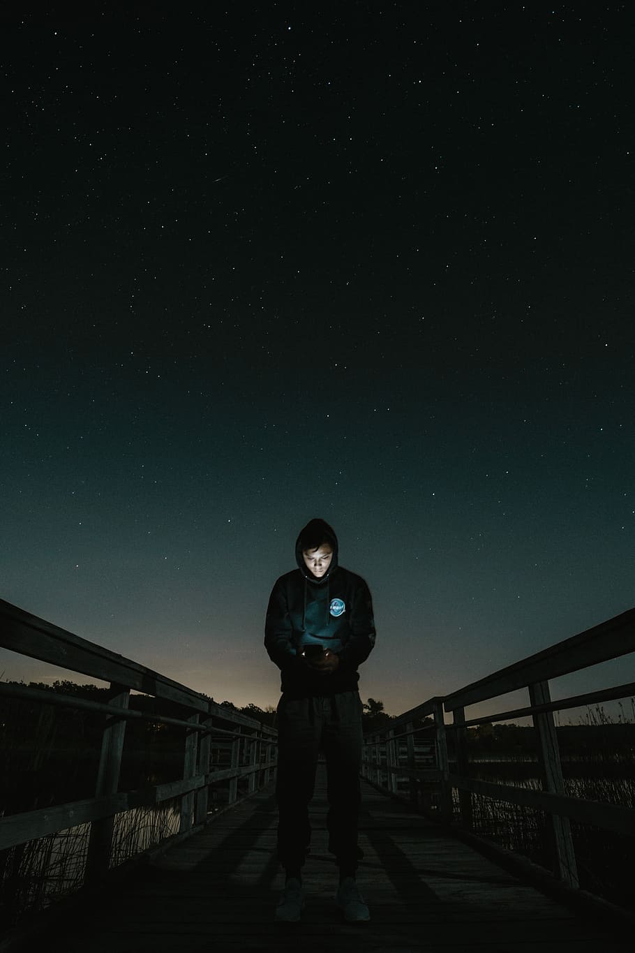 910x1365 HD wallpaper: man in the middle of bridge looking to his phone, photo of man in black hoodie standing on bridge